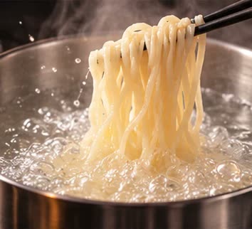 沸騰した鍋で平打ちの生麺を箸で持ち上げている